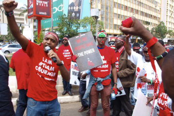 Kenyans protesting on the street, wearing red T-shirts with the text "I AM #TEAM COURAGE" and a sign saying ""WE THE PEOPLE HAVE THE POWER".
