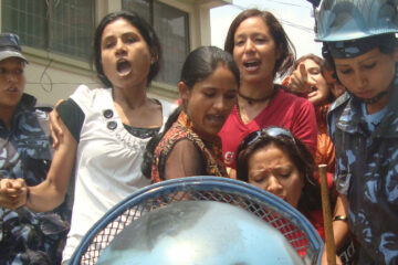 Ryhmä naisia naispuolisten mellakkapoliisien ympäröiminä auton lavalla. Etualalla poliisin kypärä..