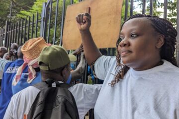 Phyllis Omido with her fist up in front of a gate together with other demonstrators.