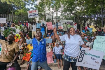 Mielenosoittajia oikeustalon edessä, mukanaan kylttejä ja megafoni. Taustalla oikeustalo ja puita.